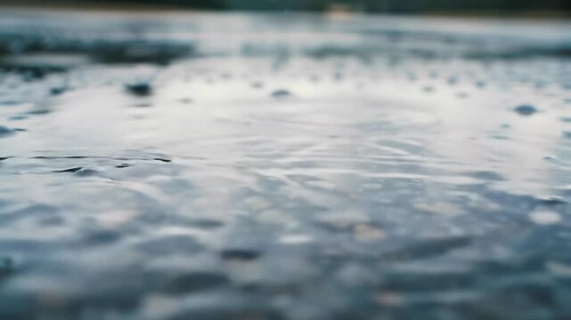 Ecu macro video of raindrops gracefully impacting dark, slick wet asphalt, creating intricate ripples and crown-like splashes, reflecting diffused light from overcast sky. Serene nature concept
