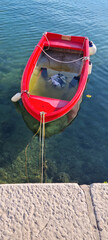 Fototapeta premium High angle view of a small red plastic rowboat filled with water and tied to a stone pier in the clear sea.