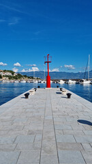 Fototapeta premium Symmetrical low angle view of a red harbor lighthouse at the end of a stone pier in Baska on Krk island Croatia.