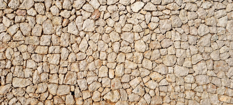 Full frame background texture of a traditional Mediterranean dry stone wall built with rough beige limestone rocks.