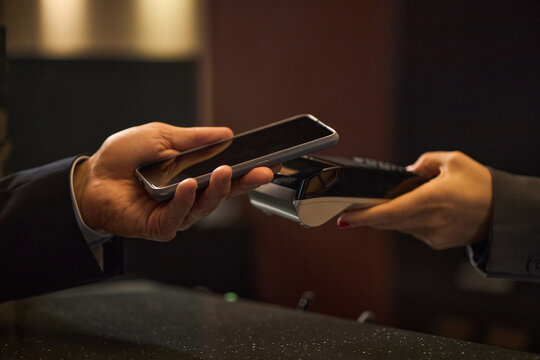 Close up of business customer holding smartphone near payment terminal, making contactless transaction at counter. Ideal for fintech, retail checkout, mobile payment marketing