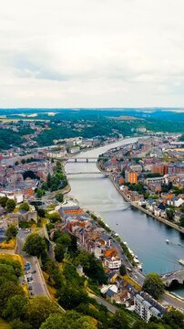 Vertical video. Namur, Belgium. the River Meuse, historic stone bridges and dense terracotta rooftops of the old town, with the massive Citadel fortress rising on its rocky promontory under soft summ