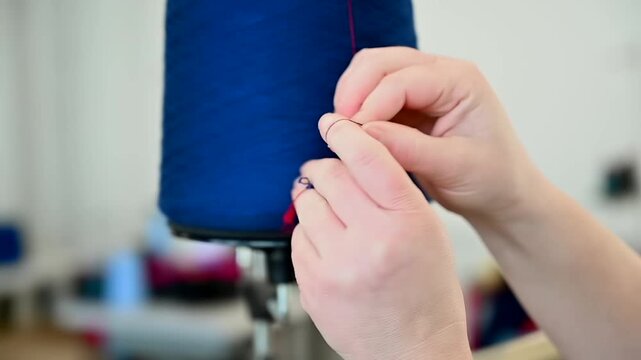 Close up of hands tying a knot in red yarn next to a large blue cone in a textile workshop.