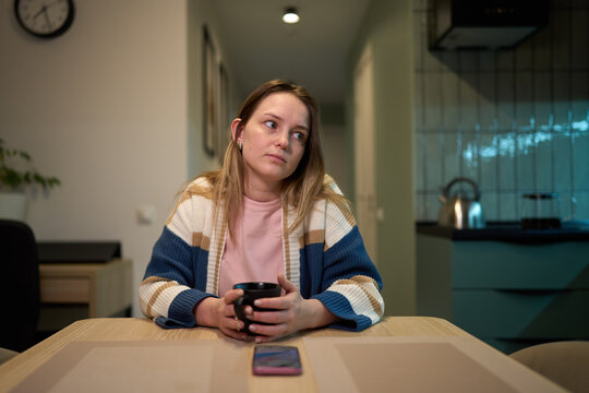 Bored young woman holding coffee mug during quiet evening at home
