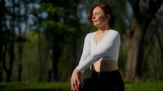 Active 45 year old woman doing dynamic hamstring stretches in sunny park