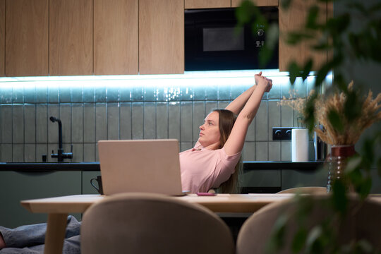 Female stretching arms at kitchen table with laptop