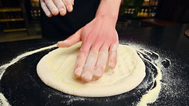 Hands knead dough on a black countertop, flour dusting visible in the kitchen