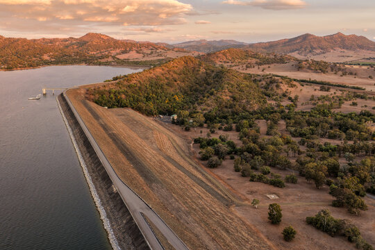 Aerial view of the Glenbawn Dam wall with surrounding water and mountain landscape in NSW Australia. Drone photograph captures the large dam structure, expansive reservoir and rugged regional scenery