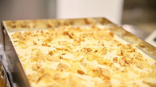 Hand sprinkling almond flakes onto carrot cake cream in a metal baking tray