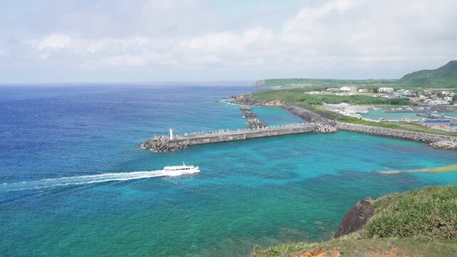 A sightseeing boat entering a port surrounded by beautiful blue ocean in Yonaguni Island, Japan's westernmost point. View from Irizaki observatory.
