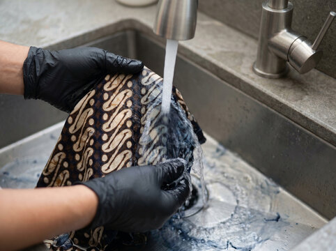 Indonesian batik cotton textile with parang motif rinsed under gentle running water from stainless faucet carrying dissolved wax traces