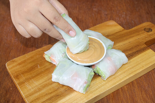 Hand dipping fresh Vietnamese spring roll into peanut sauce