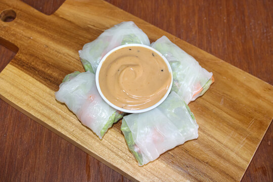 Top view of Vietnamese spring rolls with peanut sauce on wooden board