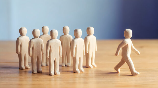 One wooden figure walks away from group of figures standing together concept individualism breaking away independence dissent unique approach leaving conformity.