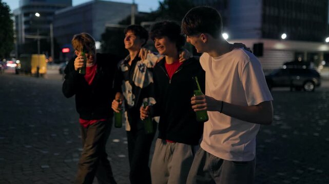 Group of four tipsy teenage friends walking and laughing on a city plaza.