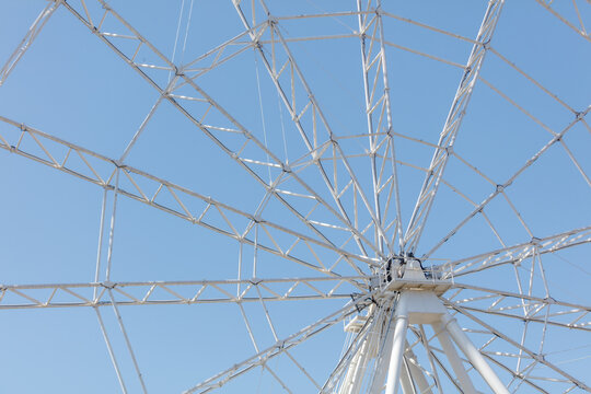 Low-angle view of giant white Ferris wheel under bright blue sky
