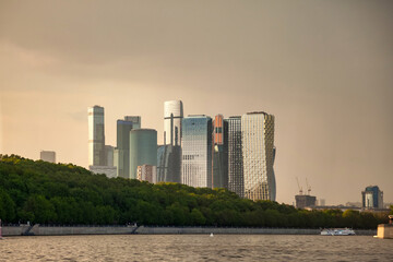 Fototapeta premium The skyline of Moscow City is viewed from the river. The modern buildings stand tall against a backdrop of clouds. The scene captures the outdoor environment on a typical day in Moscow.