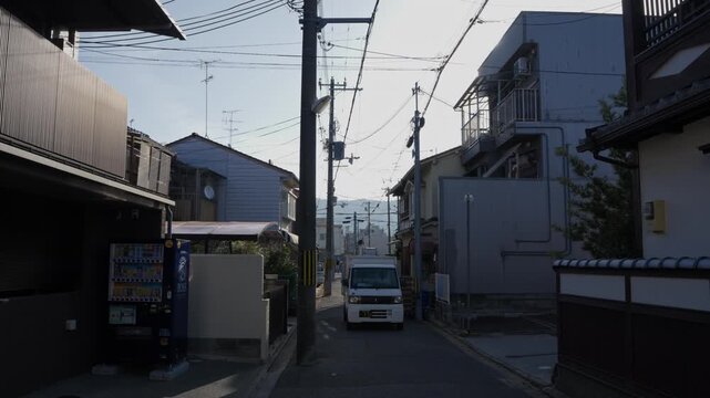 Small white kei van parked on narrow suburban street with houses and tangled power lines in Kyoto