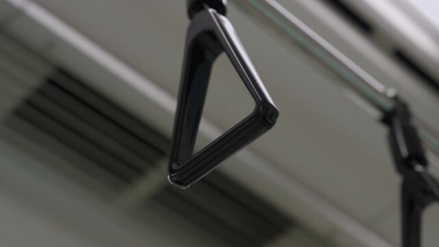 Closeup triangular passenger handle hanging from ceiling inside moving Japanese subway train