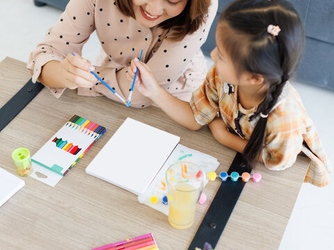 Asian happy mother help little cute daughter painting drawing at home with love enjoy quality time together affection childhood support family care nurture relationship connection motherhood leisure.