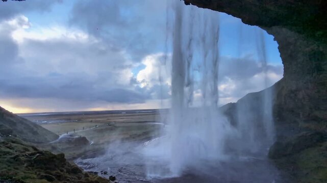 Majestic waterfall view from inside a cave, scenic mountain landscape with falling water, cinematic nature background at sunset