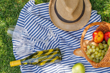 Obraz premium Picnic basket with wine, fruits, and baguette on a sunny green meadow