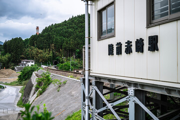 山あいを走るローカル線の線路と、その先にあるトンネルを駅舎の横から捉えた風景。 / View of rural train tracks and a tunnel in the mountains seen from the side of a station building. © Kimikatsu