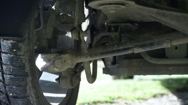 A detailed view showcases the undercarriage of a vehicle with dirt-covered parts, illuminated by the soft light of a sunny day. Nature surrounds the scene, adding tranquility.