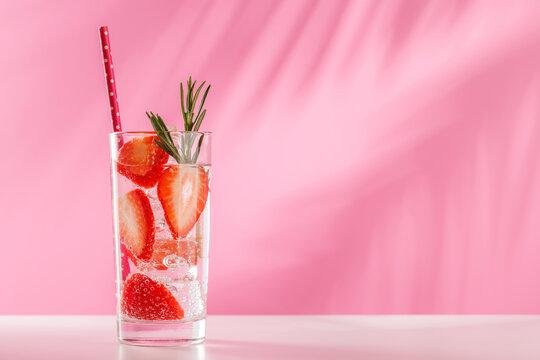 Fresh strawberry infused water with herbs on pink background with copy space