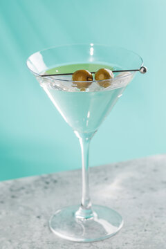 Classic martini cocktail with olives in glass on blue background