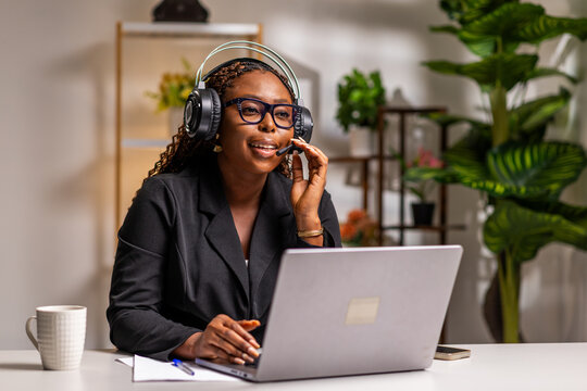 African woman working remotely with a headset and laptop in a home office