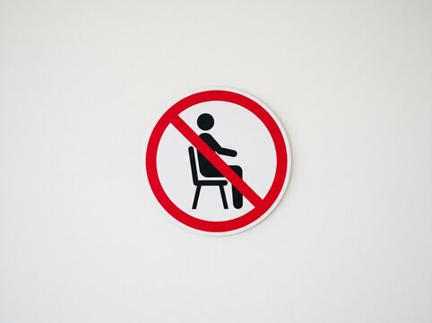 No sitting sign with a symbol of a person sitting crossed out in red on a white background, suitable for public facilities, sterile areas, and public prohibition designs.