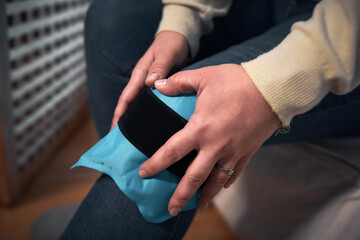 Obraz premium Woman at home holding painful injured knee with a cold gel ice pack.