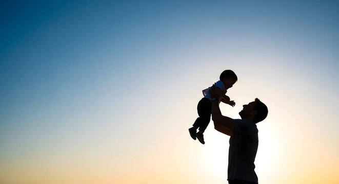 Silhouette of a father lifting his baby son against sunset sky