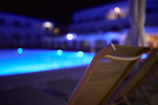 Glowing swimming pool in a luxury resort at night with blue illuminated water and soft background blur.