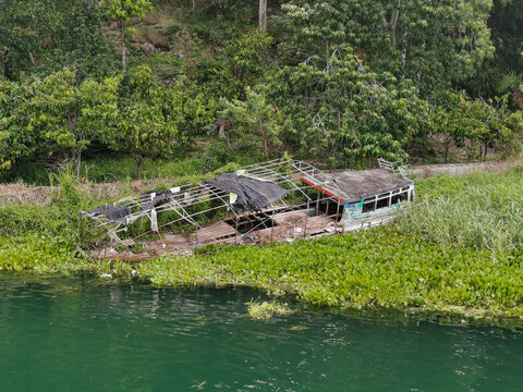 Abandoned wooden boat overgrown by vegetation on the shore of Lake Toba, Indonesia, surrounded by lush tropical greenery and calm turquoise water.