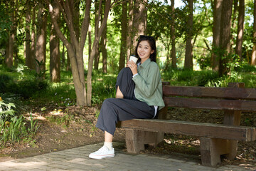 Fototapeta premium Smiling Young Woman Holding Coffee Cup on Park Bench