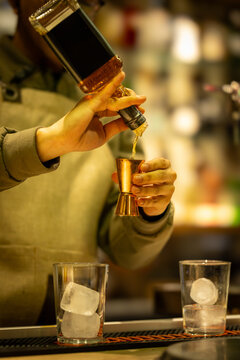 Bartender measuring liquor with metallic jigger while preparing cocktails at illuminated bar counter, concept of handcrafted mixology, modern hospitality and nightlife.