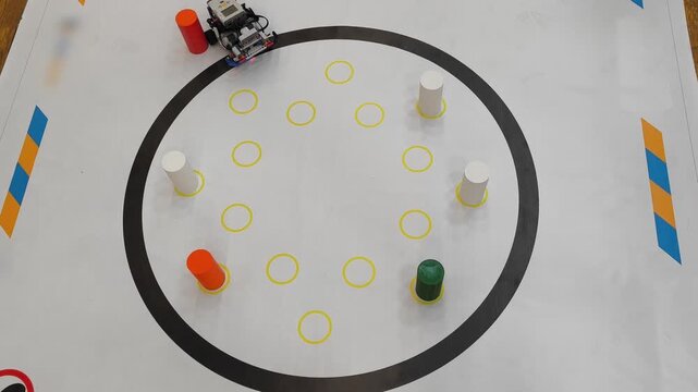 Top view - a robot works in a circular area with colored cylinders on a competition field for robotics, STEM, programming.
