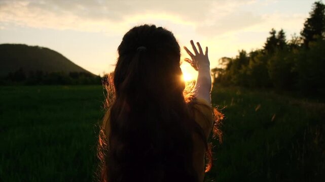 Dreaming child pulls hands to sun. Religion helping hand. Preteen girl enjoy beautiful summer nature during epic warm sunset or sunrise. Prayer in religion concept