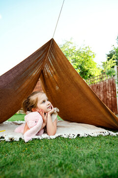 Little girl relaxing in backyard tent with her comforting toy