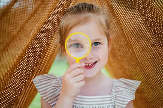 Little girl with magnifying glass in a blanket tent outdoors