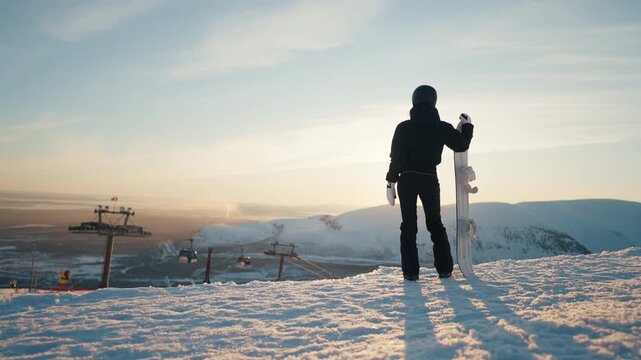 Be at top, conquer summit and get goal, woman snowboarder admiring mountains. Back view of sportswoman with snowboard standing on peak of mount and watching picturesque landscape with ski resort