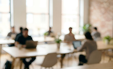 Obraz premium A blurred image of a modern coworking space featuring several individuals working on laptops amidst a bright, open atmosphere with plants.