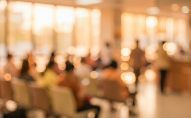Fototapeta premium A blurred image of a hospital waiting room, filled with patients sitting in chairs during a sunny afternoon, creating a warm, busy atmosphere.