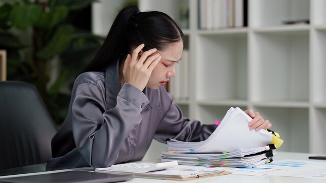 Stressed Asian businesswoman overwhelmed by paperwork in office
