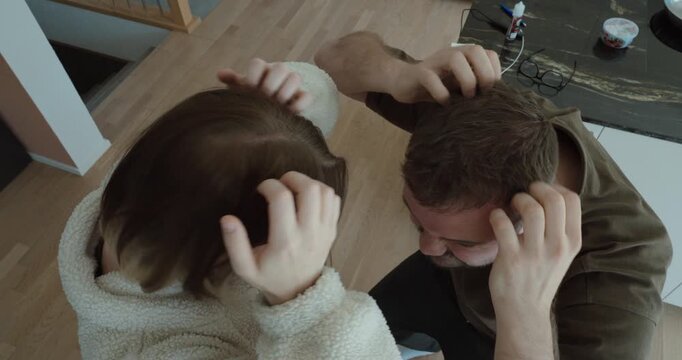 Top view of two people scratching their heads, illustrating itchy scalp caused by lice infestation, hygiene issues, or skin irritation in a home environment.