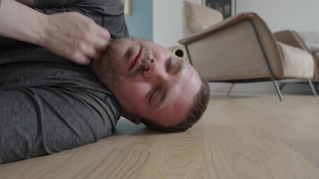 Close-up of an unconscious man lying on the floor while a person checks his pulse and opens his airway, illustrating first aid response and emergency situation at home.