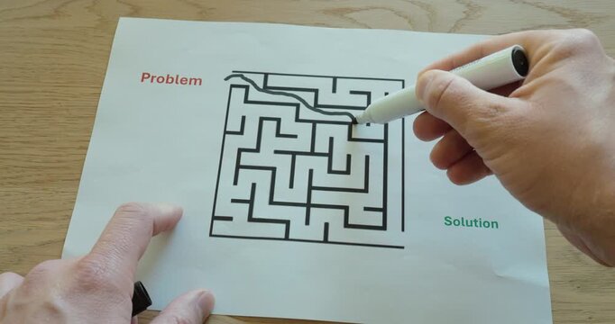 Close-up of hands solving a printed maze labeled problem and solution using a marker. Visual metaphor for problem solving, strategy, decision making, and finding the right path in business or everyday