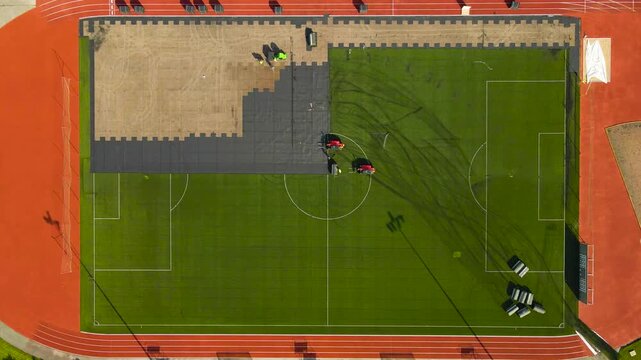Top down aerial view of construction workers installing a new artificial turf on a soccer pitch surrounded by a running track